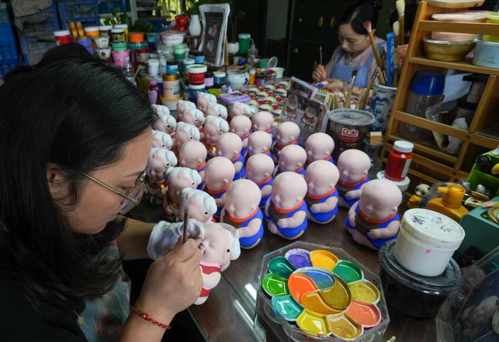 A craftswoman paints Huishan clay figurines by hand in a Wuxi workshop surrounded by colorful pigments.