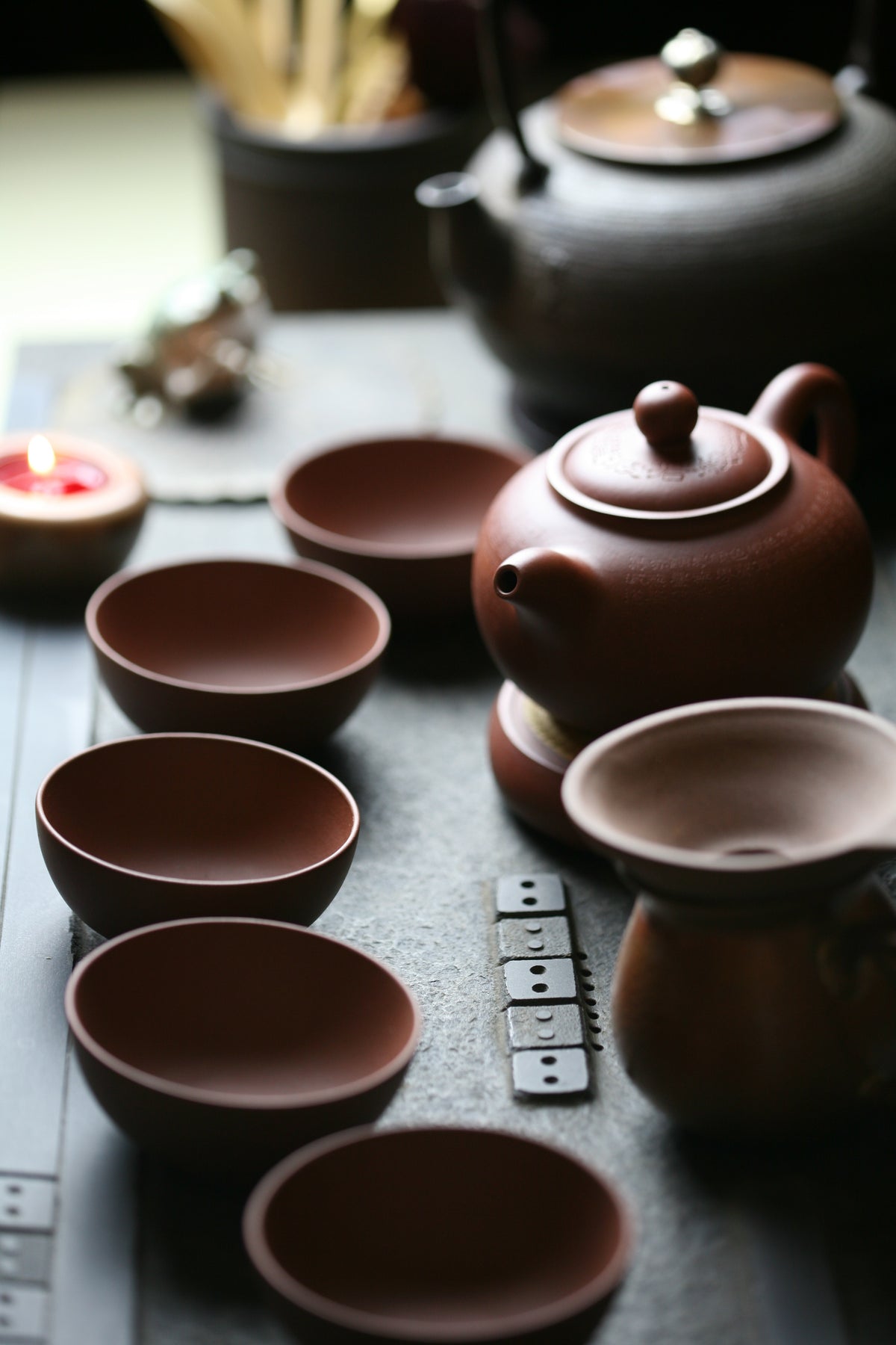A reddish-brown Yixing clay teapot surrounded by small tea bowls on a tea tray.
